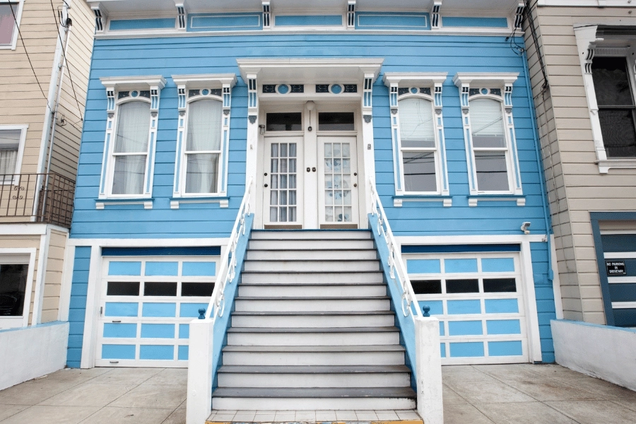 bright blue duplex with two garages and white front doors next to each other in a city